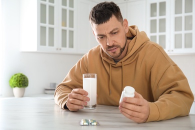 Photo of Man taking medicine for hangover at table in kitchen