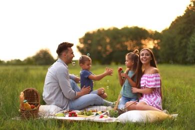 Happy family having picnic in park at sunset