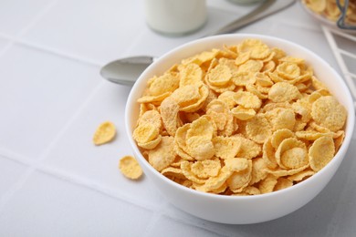 Photo of Breakfast cereal. Tasty crispy corn flakes in bowl on white tiled table, closeup. Space for text