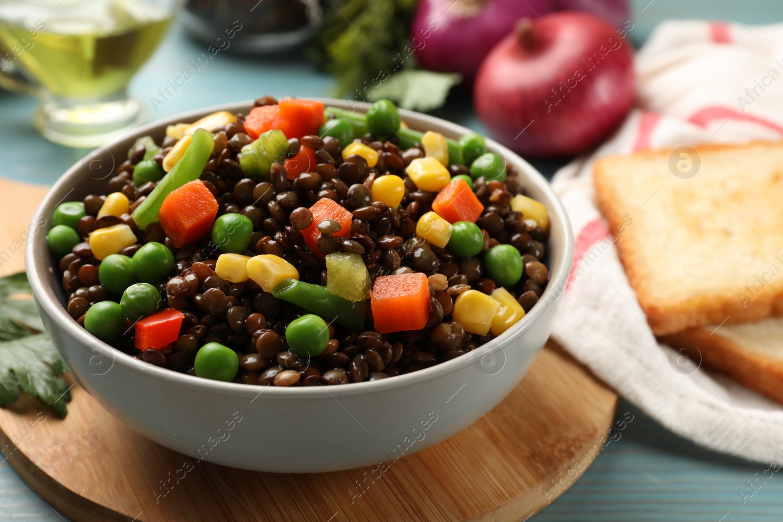 Photo of Delicious lentils with vegetables in bowl on light blue table, closeup