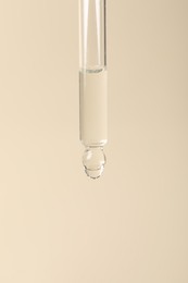 Dripping cosmetic serum from pipette on beige background