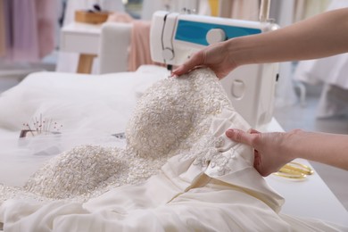 Photo of Dressmaker creating beautiful wedding dress with embroidered bustline and bow at table in workshop, closeup