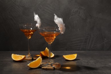 Photo of Tasty cocktails in glasses decorated with cotton candy and orange slices on gray table, space for text