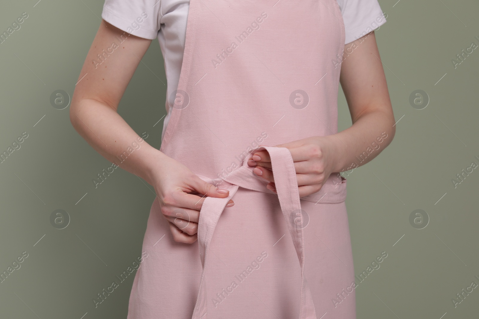 Photo of Woman putting on pink apron against light green background, closeup