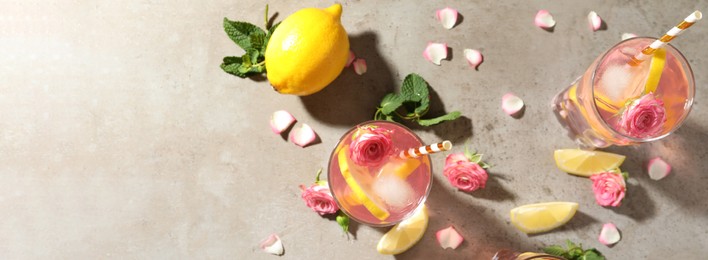 Image of Delicious refreshing drink with rose flowers and lemon slices on light grey table, flat lay with space for text. Banner design