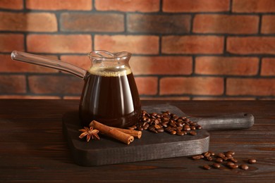 Glass turkish coffee pot with hot drink, beans and spices on wooden table