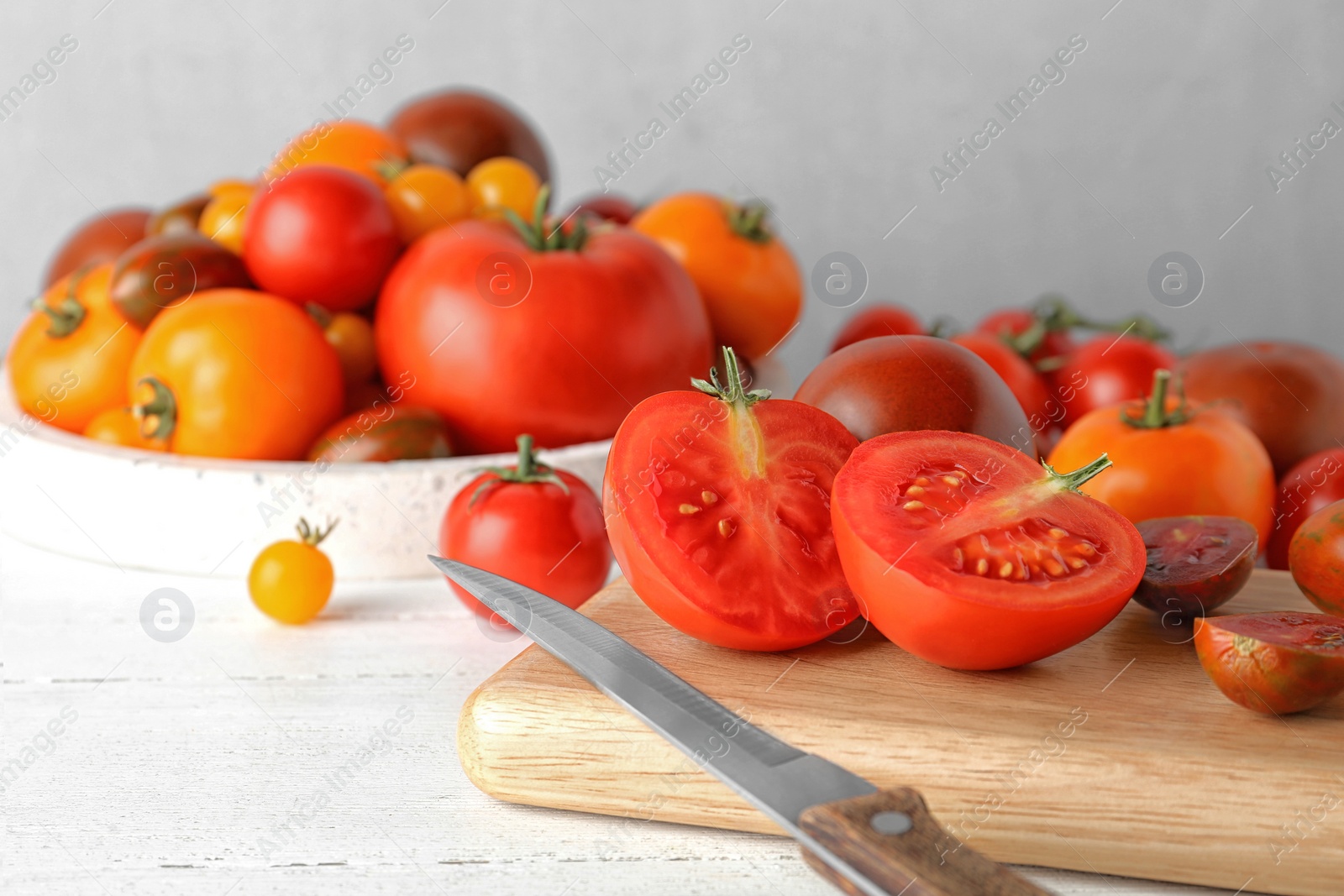 Photo of Fresh ripe tomatoes, cutting board and knife on white wooden table