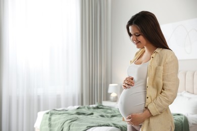 Young happy pregnant woman in bedroom, space for text