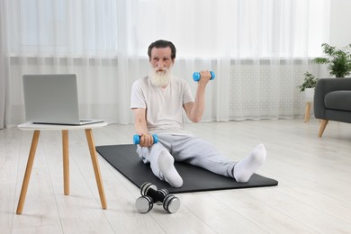 Photo of Senior man exercising with dumbbells while watching online tutorial at home. Sports equipment