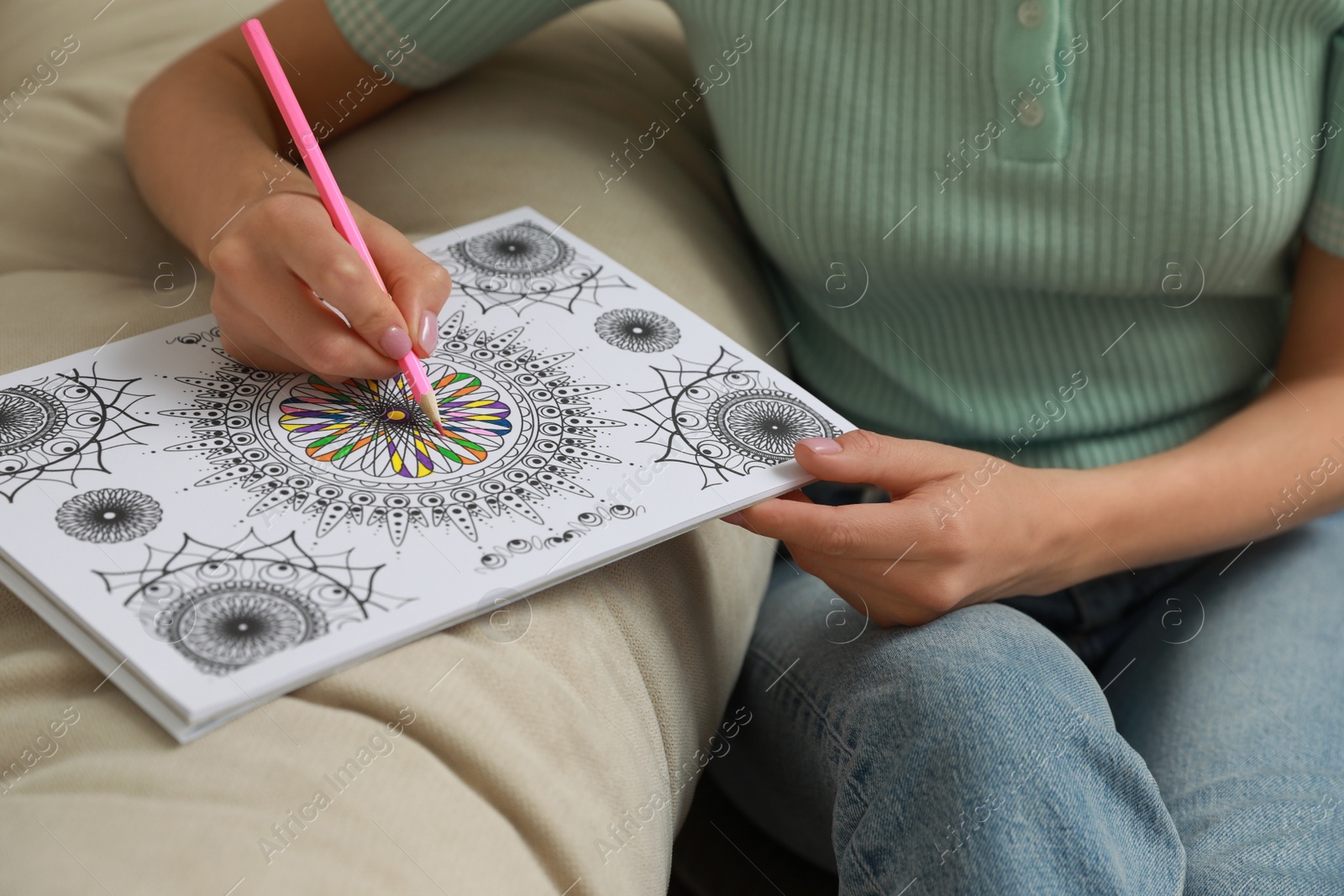 Photo of Young woman coloring antistress page near sofa, closeup