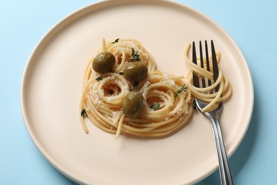 Photo of Heart made of tasty spaghetti, fork, olives and cheese on light blue background, closeup