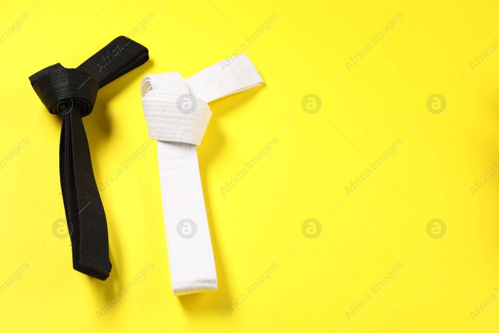 Photo of Black and white karate belts on yellow background, flat lay. Space for text