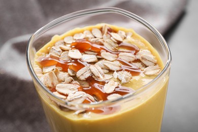 Glass of delicious smoothie with oat flakes and caramel syrup on grey table, closeup