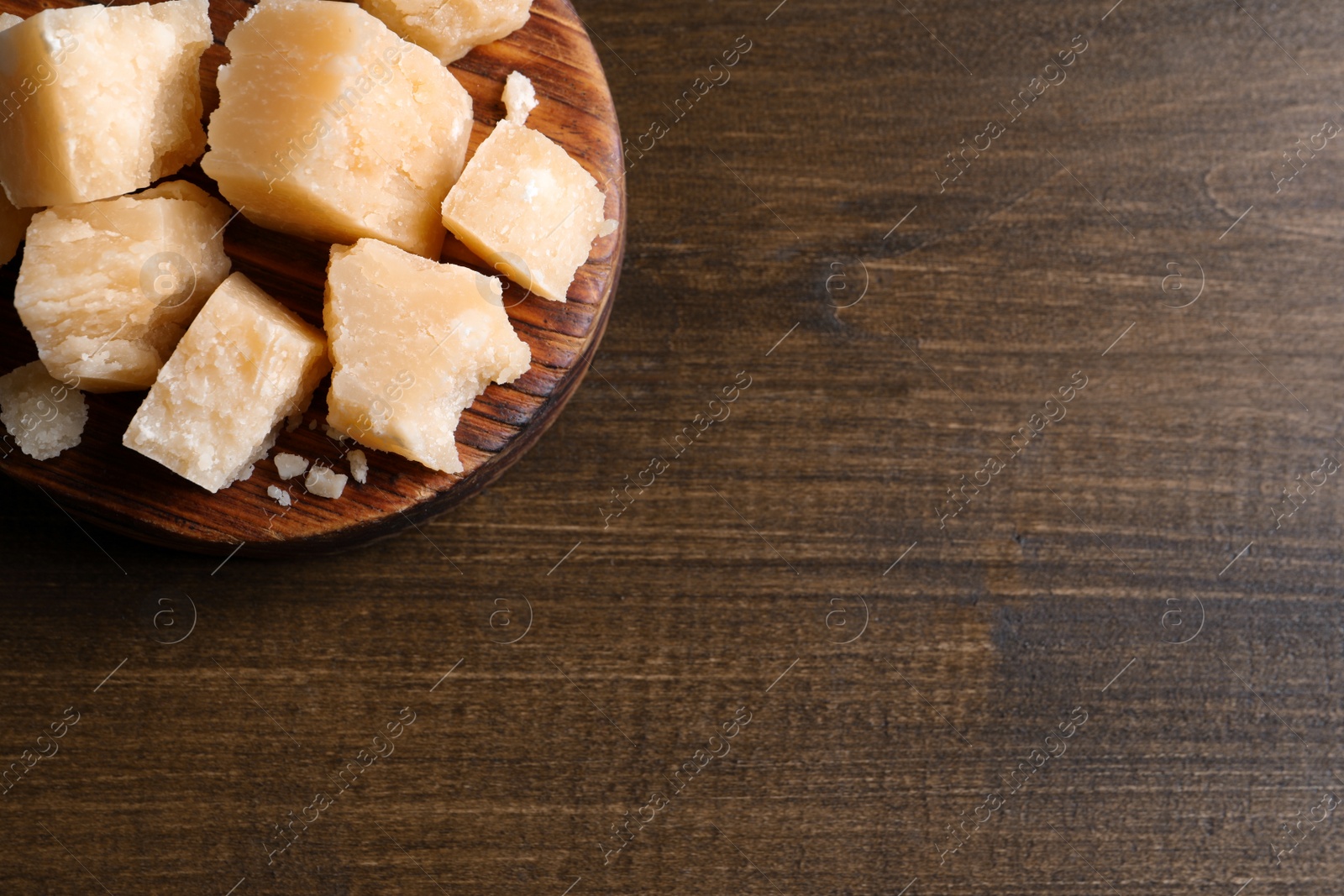 Photo of Pieces of delicious parmesan cheese on wooden table, top view. Space for text