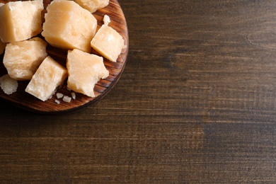 Photo of Pieces of delicious parmesan cheese on wooden table, top view. Space for text