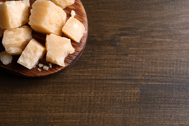 Pieces of delicious parmesan cheese on wooden table, top view. Space for text