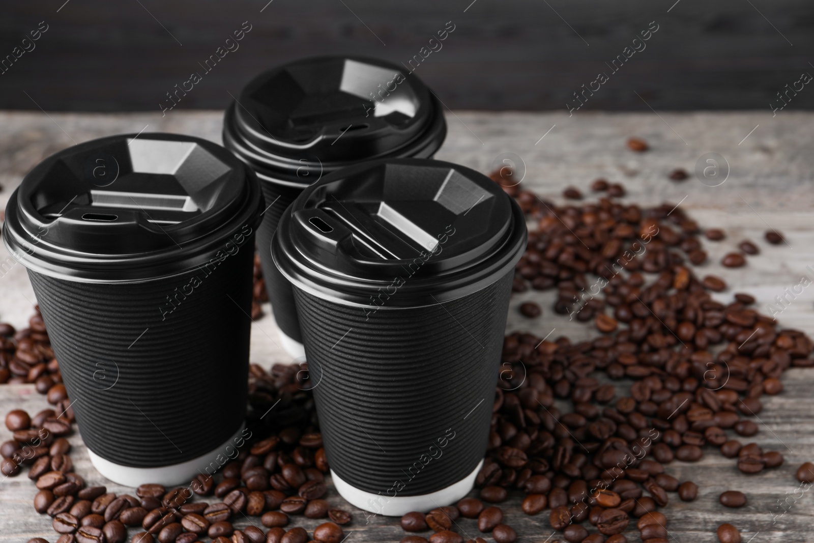Photo of Coffee to go. Paper cups and roasted beans on wooden table, closeup. Space for text
