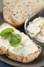 Photo of Pieces of bread with cream cheese and basil leaves on gray plate, closeup