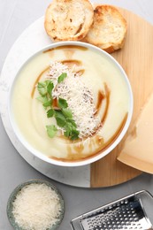 Delicious cream soup with parmesan cheese, soy sauce in bowl and croutons on light grey table, flat lay