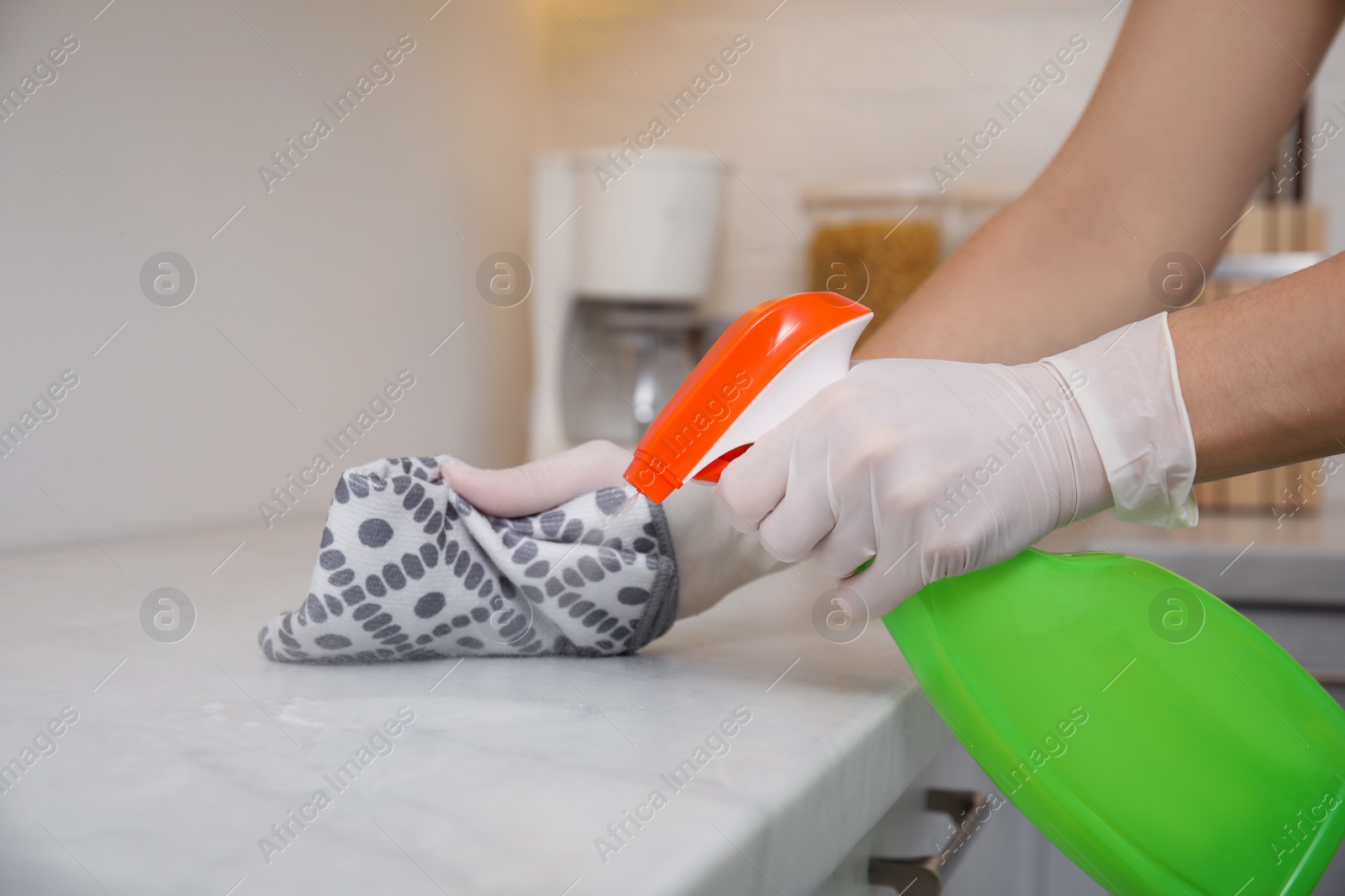 Photo of Woman cleaning white marble countertop with rag and detergent in kitchen, closeup