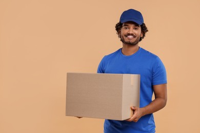 Photo of Happy young courier with parcel on light brown background, space for text