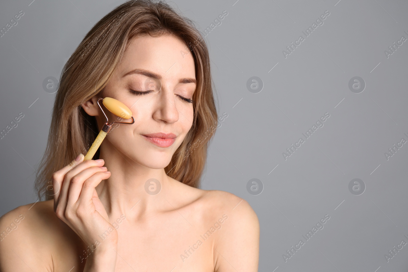 Photo of Young woman using natural jade face roller on light grey background