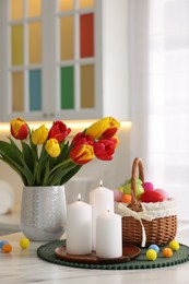 Photo of Easter decorations. Bouquet of tulips, painted eggs and burning candles on table indoors