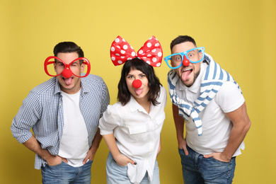 Group of friends with funny accessories on yellow background. April fool's day