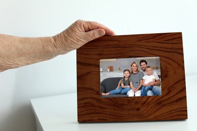 Elderly woman with framed photo portrait of her family indoors, closeup