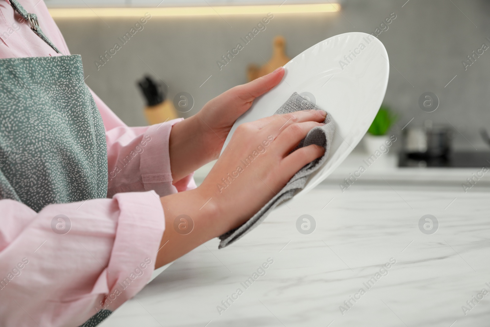 Photo of Woman wiping plate with towel at white marble table in kitchen, closeup