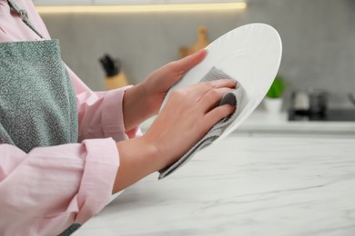 Photo of Woman wiping plate with towel at white marble table in kitchen, closeup
