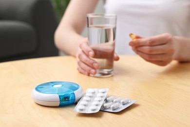 Woman with pills, organizer and glass of water at light wooden table, selective focus