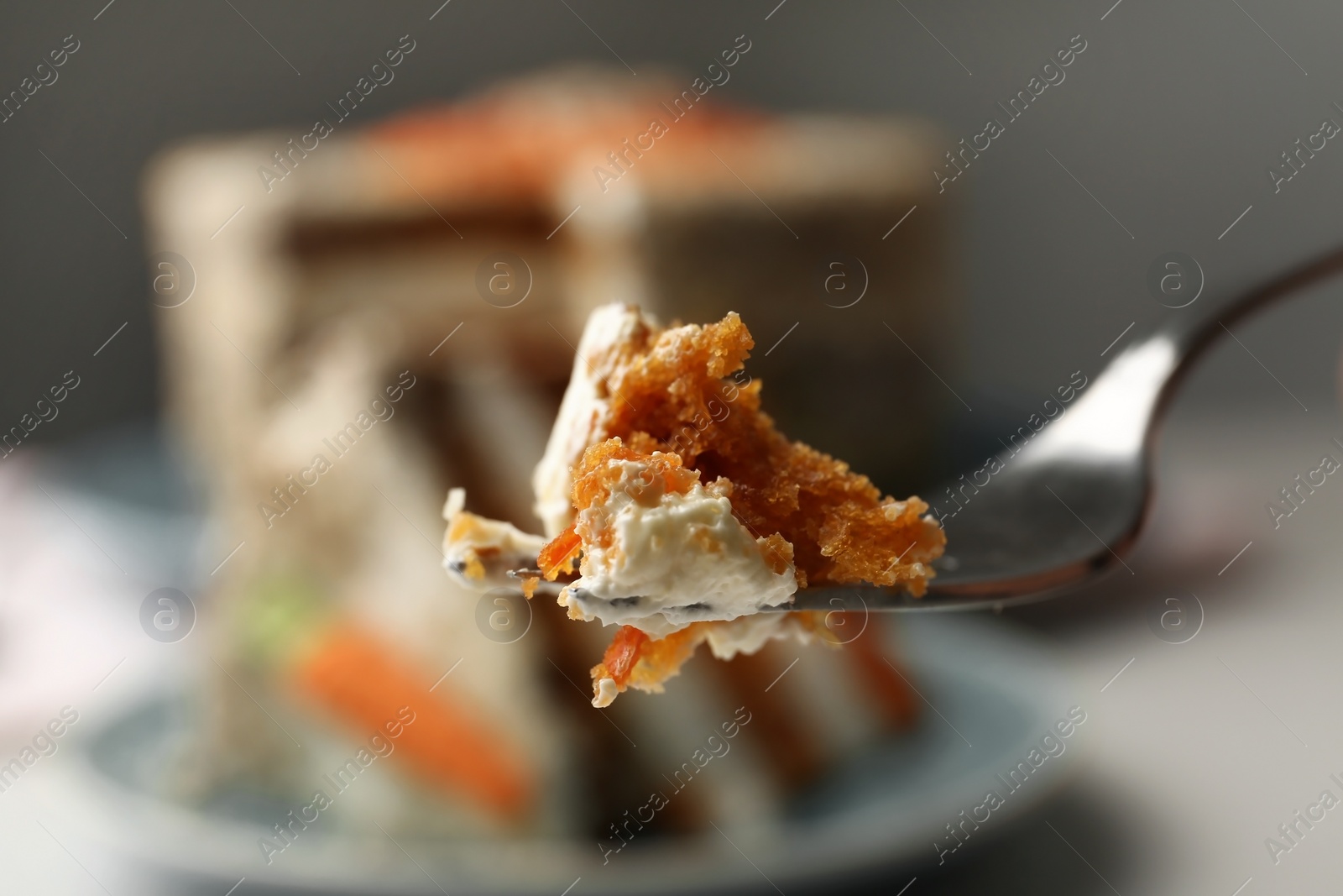 Photo of Fork with piece of carrot cake against blurred dessert, closeup