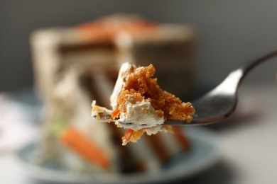 Fork with piece of carrot cake against blurred dessert, closeup