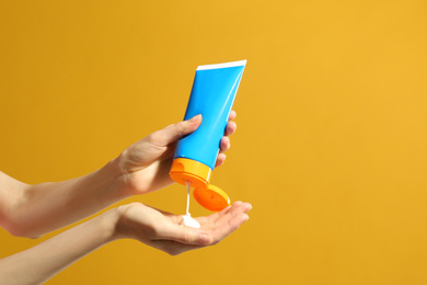 Photo of Woman applying sun protection cream on hand against yellow background, closeup. Space for text