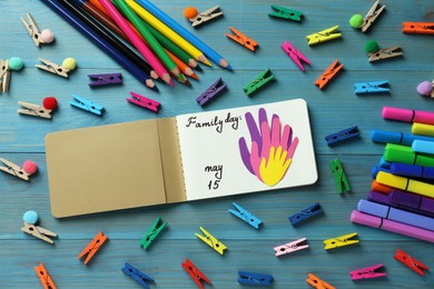 Photo of Notebook with text Family Day May 15 and paper cutout surrounded by colorful stationery on light blue wooden table, flat lay