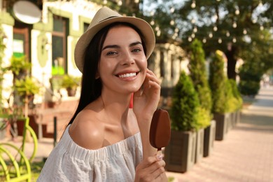 Photo of Beautiful young woman holding ice cream glazed in chocolate on city street