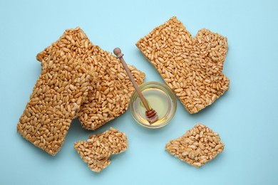 Photo of Puffed rice bars (kozinaki) and honey on light blue background, flat lay