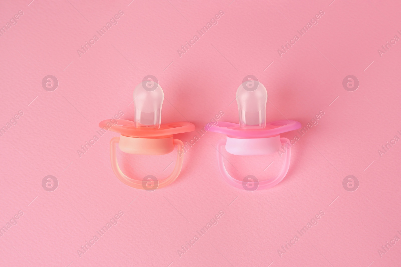 Photo of New baby pacifiers on pink background, flat lay