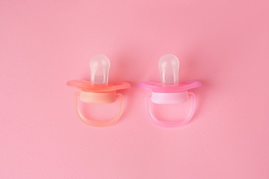 Photo of New baby pacifiers on pink background, flat lay