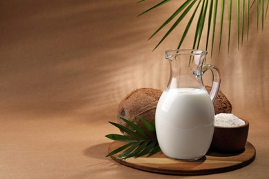 Glass jug of delicious vegan milk, coconuts, flakes and palm leaf on brown background. Space for text