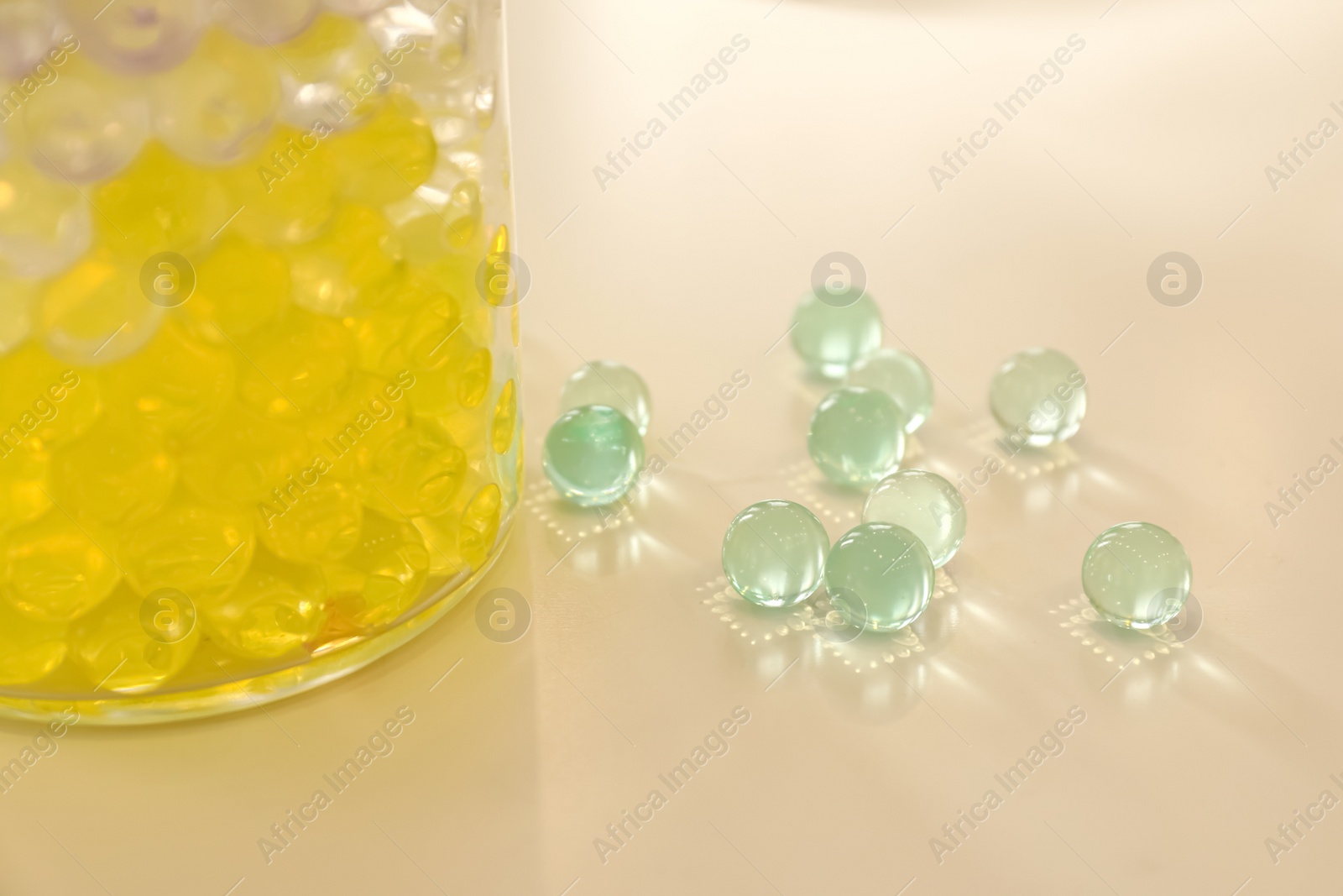 Photo of Different color fillers and glass vase on white table, closeup. Water beads