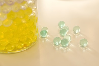 Photo of Different color fillers and glass vase on white table, closeup. Water beads