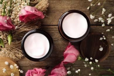 Photo of Jars of face cream and beautiful flowers on wooden table, flat lay