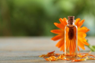 Photo of Bottle of essential oil with calendula extract and flower petals on wooden table outdoors, closeup. Space for text