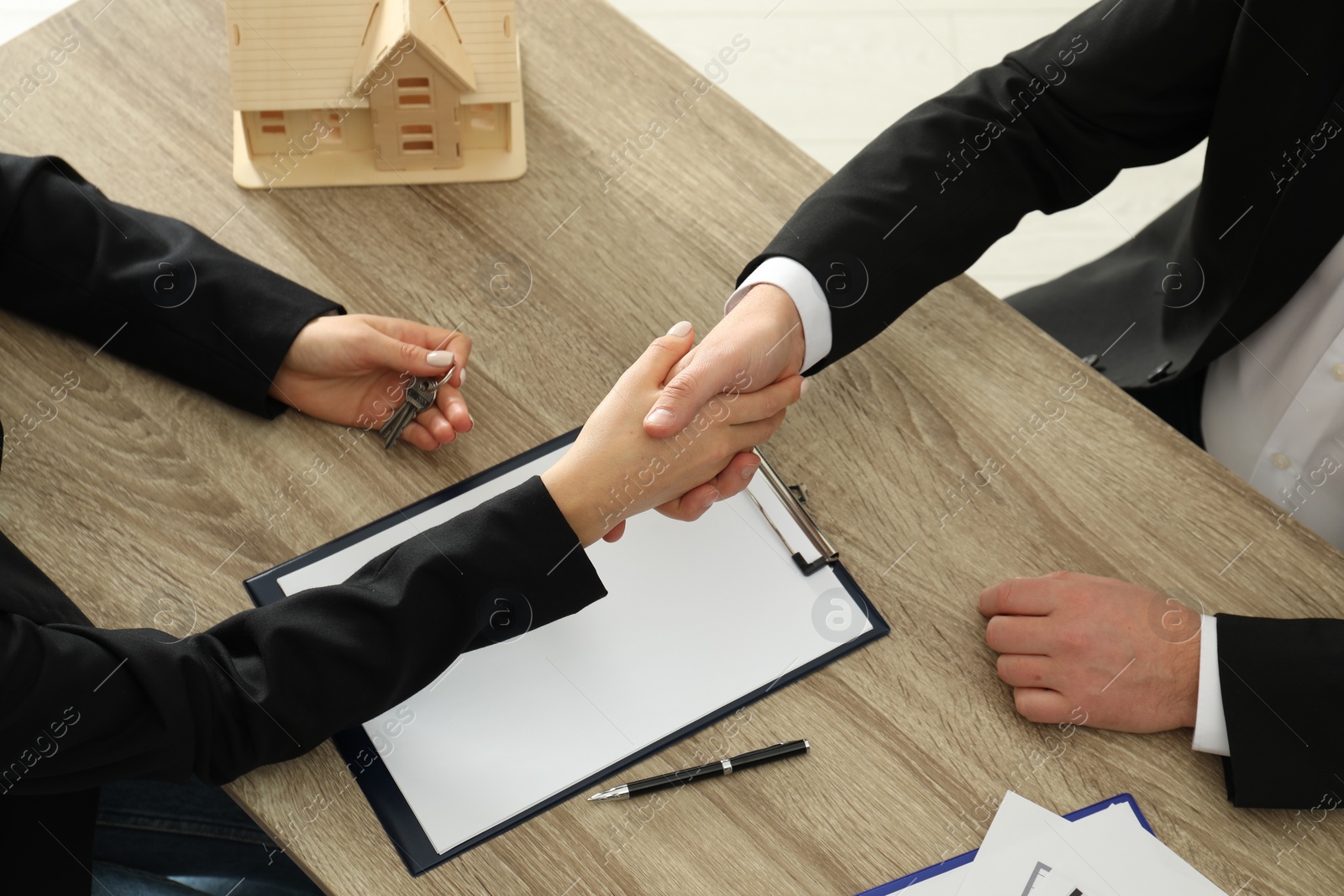 Photo of Real estate agent shaking hands with client at table in office, above view