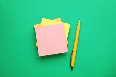 Photo of Colorful empty notes and pen on green background, flat lay