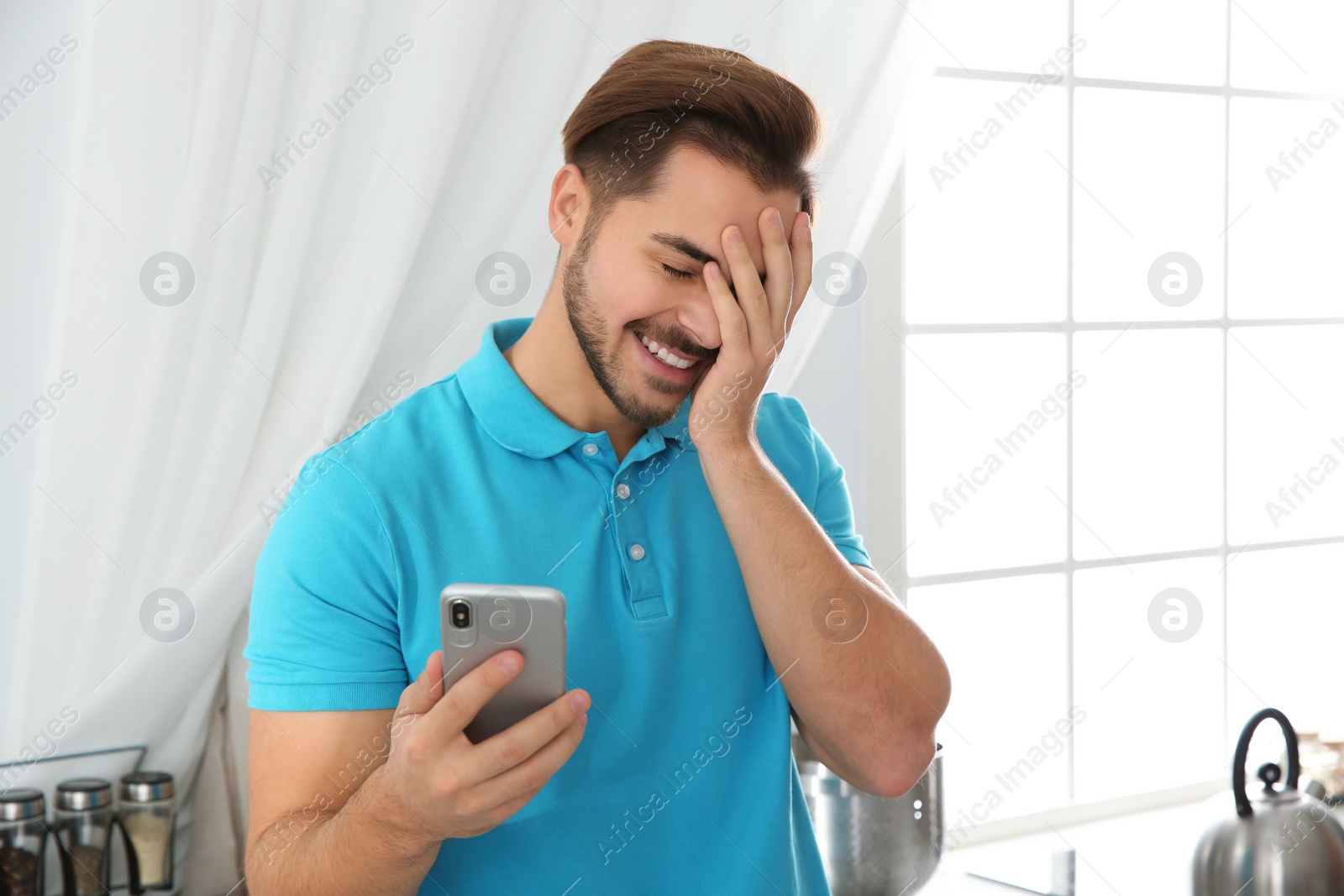 Photo of Young man laughing while using smartphone at home