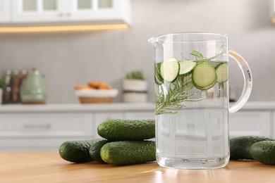 Photo of Refreshing cucumber water with rosemary in jug and vegetable on wooden table, closeup. Space for text