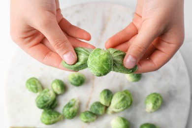 Photo of Woman separating leaves from fresh brussel sprouts at white table, closeup